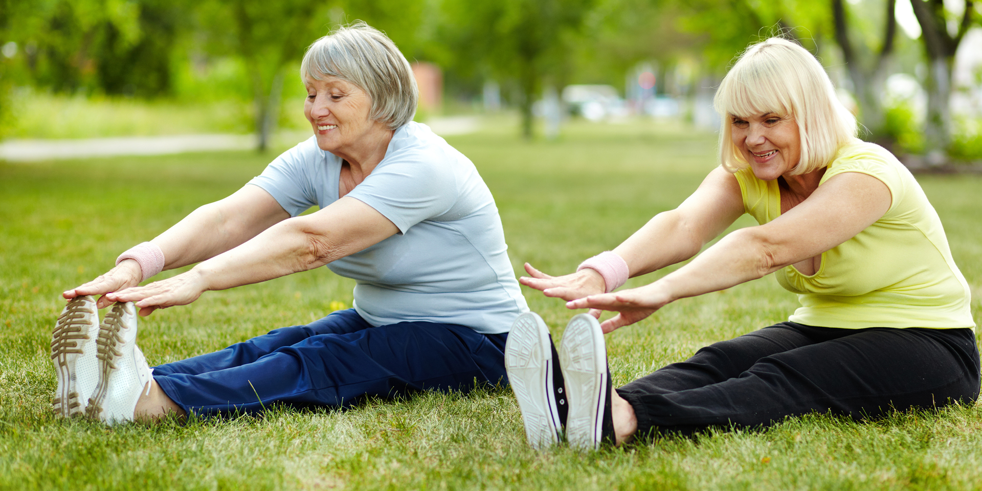 two older women sitting in the grass touching their toes